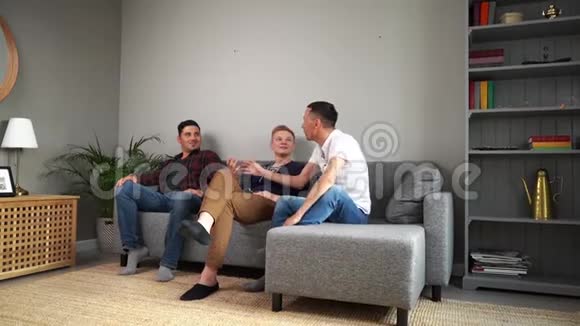 三个年轻的成年朋友坐在柔软的沙发上无忧无虑地交流视频的预览图