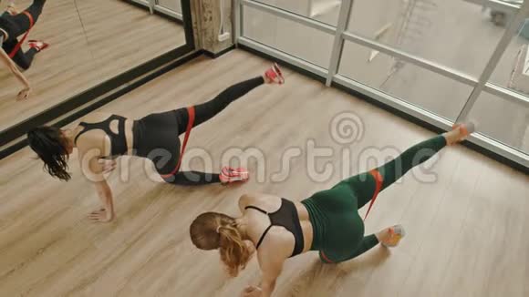 两个女人在工作室里用大腿之间的拉伸皮带训练腿站在膝盖上拉着腿视频的预览图