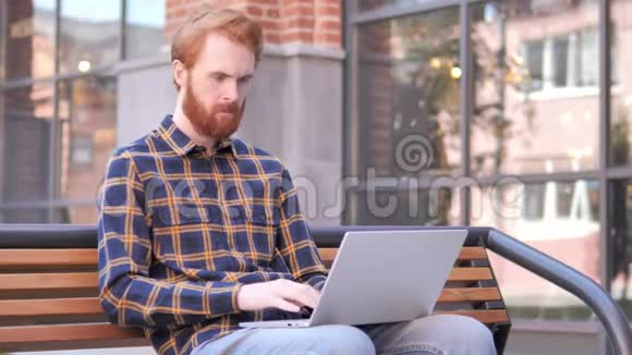 红头发的胡子男青年在笔记本电脑上庆祝视频的预览图