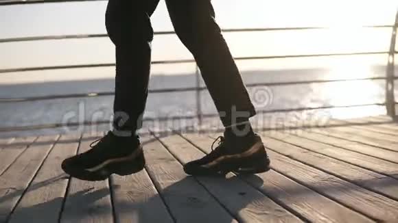 有目标的男腿舞蹈镜头现代嘻哈由穿着黑色运动鞋的男子在清晨的海面上表演视频的预览图