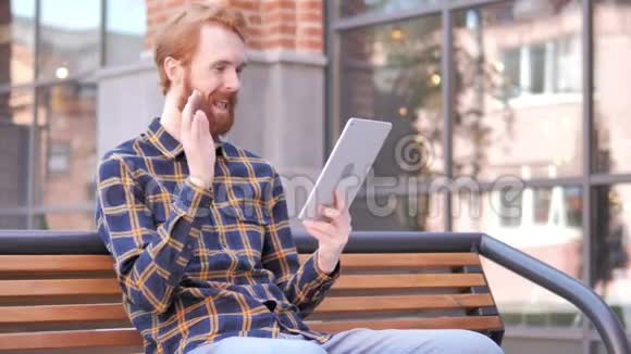 红胡子青年坐在长凳上的视频聊天视频的预览图