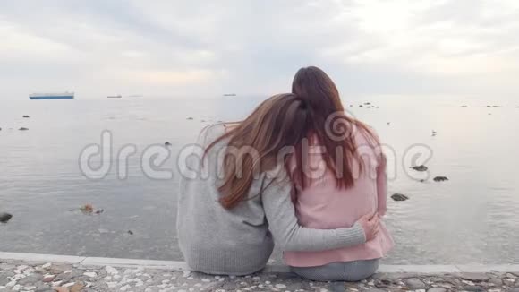 两个年轻的女人拥抱坐在靠近大海的楼梯上看着水视频的预览图