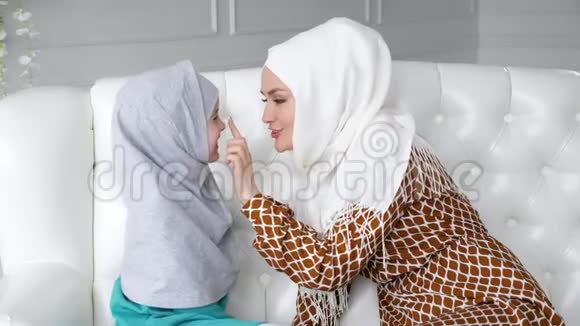 穆斯林家庭的妈妈和女儿戴着头巾坐在沙发上妈妈亲吻着女孩的手视频的预览图