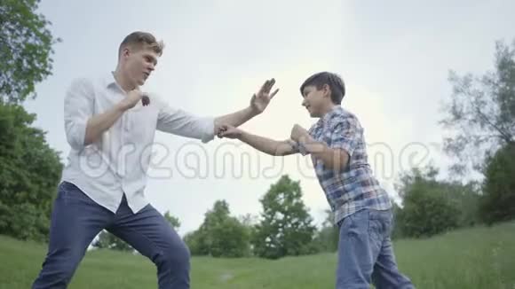 年轻人和公园里的男孩拳击年轻的父亲模仿拳打脚踢他的儿子也这样做家庭休闲视频的预览图