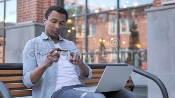 坐在长凳上的非洲男人成功的网上购物视频的预览图