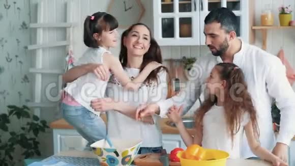 父母和两个女儿在厨房做饭他们拥抱和笑慢动作视频的预览图