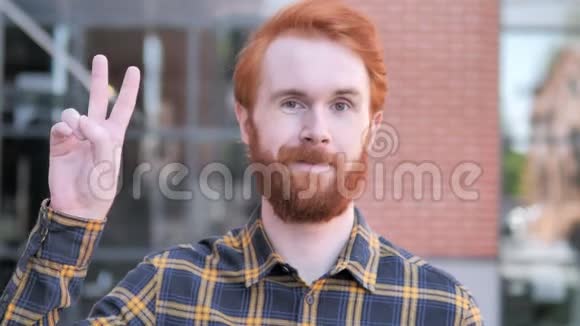 红胡子青年站在户外的胜利标志视频的预览图
