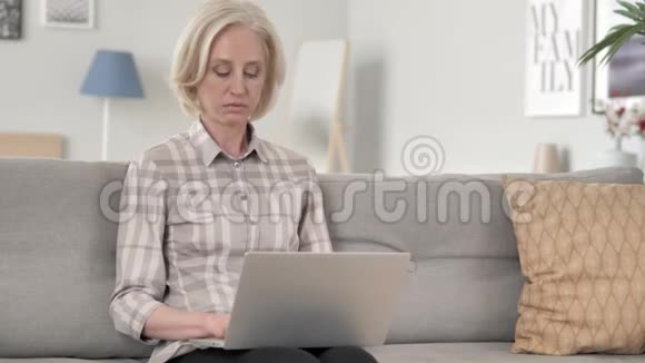 坐在沙发上用笔记本电脑的老年妇女视频的预览图