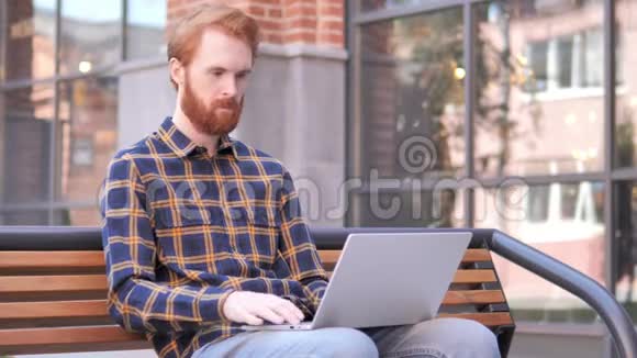 红胡子青年坐在长凳上的在线视频聊天视频的预览图