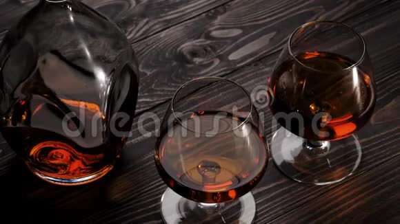 豪华白兰地手从左边从木桌上拿两个玻璃杯中的一个白兰地白兰地嗅探器狂欢慢动作视频的预览图
