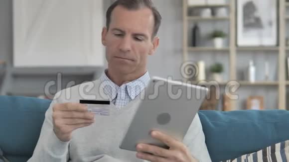 坐在沙发上的中年男子在餐桌上的网上购物视频的预览图