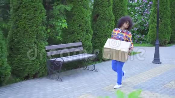 笨拙的非洲裔美国妇女有非洲发型他走在街上手里拿着一个盒子把它掉了下来视频的预览图