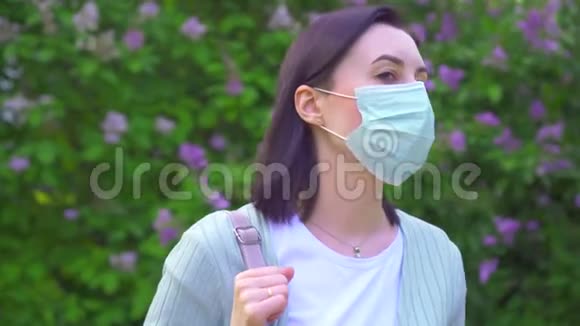 公园里开花植物背景上戴着医用面具的年轻女子的肖像视频的预览图