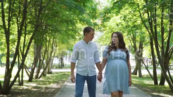 男人和他怀孕的妻子在夏天公园散步视频的预览图