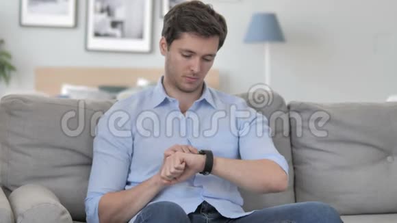 坐在沙发上用智能手表的帅哥视频的预览图