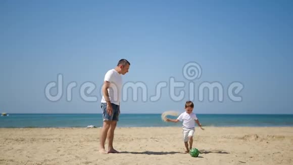 快乐的一家人爸爸和他的儿子在沙海岸边玩足球动作很慢视频的预览图