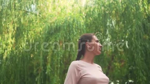 在绿柳的背景下公园里怀孕的女孩平静的女孩站在公园里双手抱着她的肚子视频的预览图
