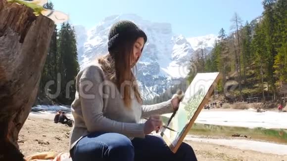 白云石一个穿着黑色帽子和灰色毛衣的年轻女子在大自然中画一幅画视频的预览图