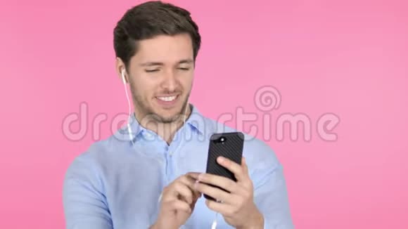 粉红背景下在智能手机上跳舞的年轻人听音乐视频的预览图