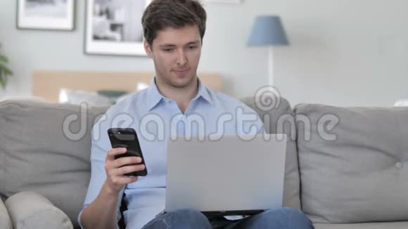 年轻帅哥上班用智能手机坐在沙发上视频的预览图