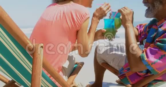 活跃的非洲裔美国老年夫妇在4k海滩躺椅上喝鸡尾酒侧视图视频的预览图