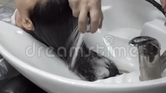 理发师在理发店白色的地上用淋浴间流出的浓水给女孩洗头视频的预览图
