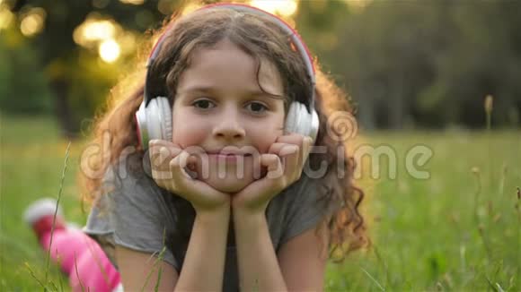 女孩躺在草地上听音乐在耳机上可爱的小白种人的孩子正在享受快乐视频的预览图