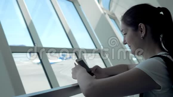 年轻女子正在看手机屏幕等待她在机场的航班视频的预览图