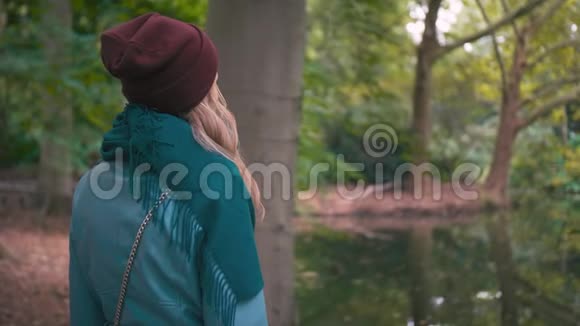 一个未被认出的年轻女子戴着红色帽子和蓝色夹克秋天在湖边的公园里拉着视频的预览图