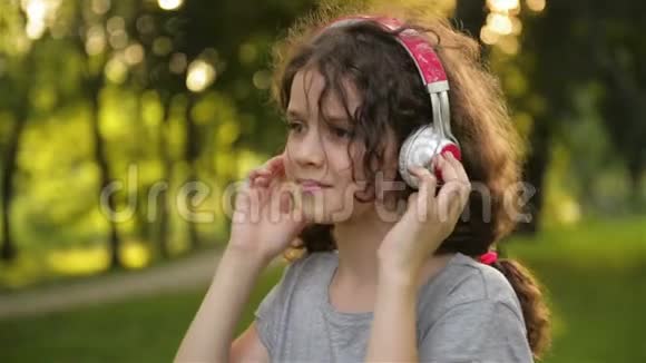 女孩躺在草地上听音乐在耳机上可爱的小白种人的孩子正在享受快乐视频的预览图