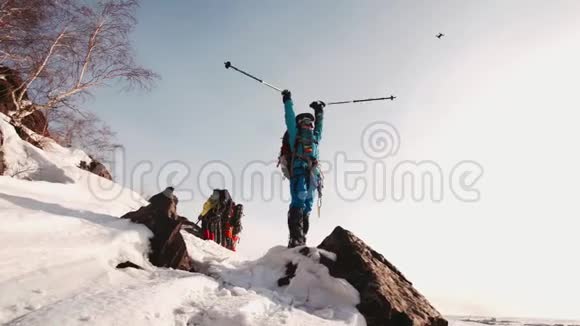 女孩登山者站在山上的岩石上她举起双手把滑雪杆放在一边在背景中是视频的预览图