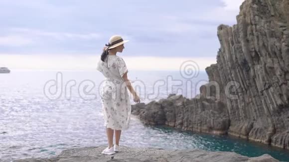 岩石海岸上美丽的景色一位戴着帽子穿着轻便衣服的美女站在悬崖边上视频的预览图