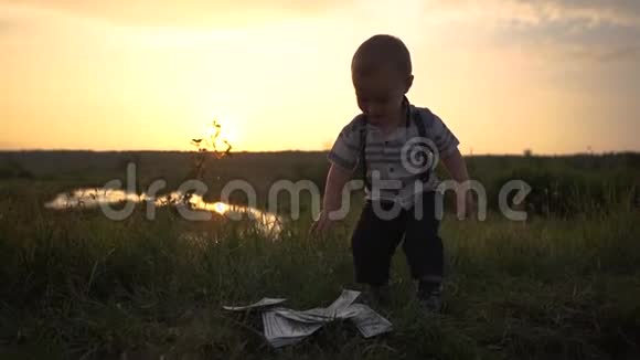 一个小男孩高兴地在户外缓慢地扔出一大叠美元钞票视频的预览图