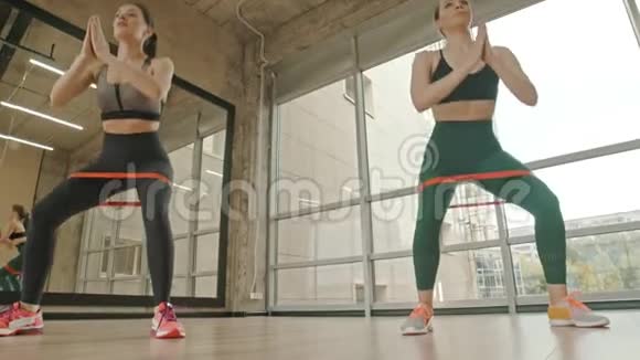 两个健康的女人用大腿之间的伸展带训练她们的腿蹲视频的预览图
