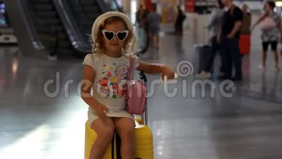 小女孩游客坐在火车站的一个大黄色手提箱上儿童正在等待出发前往视频的预览图