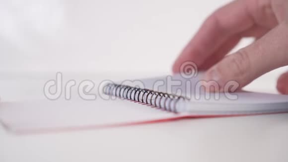 一个年轻人慢慢地翻阅一本笔记本笔记本上有螺旋形的水平页贴在白色的背景上视频的预览图