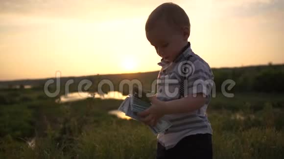 可爱的宝宝扔了一大叠美元钞票在日落时自然存在视频的预览图