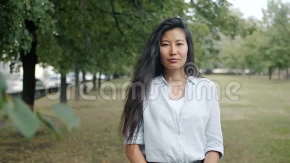 一个迷人的亚洲女人在夏天独自站在绿色公园微笑的肖像视频的预览图