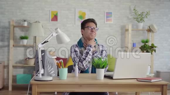 穿着衬衫的冷酷的亚洲年轻人用喷雾剂治疗坐在笔记本电脑前的喉咙痛视频的预览图