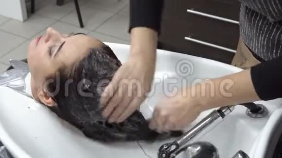 头发护理理发师在理发店用白色洗面盆洗发水理发后女孩的头视频的预览图