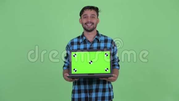 快乐的年轻人留着胡子的波斯时髦男人一边说着一边展示着笔记本电脑视频的预览图