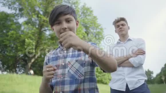 那个男孩在夏天公园里对着镜头吹着空气他哥哥的父亲站在后台视频的预览图