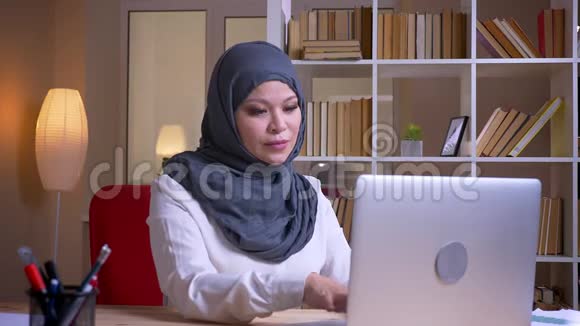 成年穆斯林成功女商人在笔记本电脑上打字并兴奋地微笑的特写镜头视频的预览图