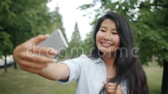 美丽的亚洲女孩用智能手机相机在户外自拍的慢动作视频的预览图