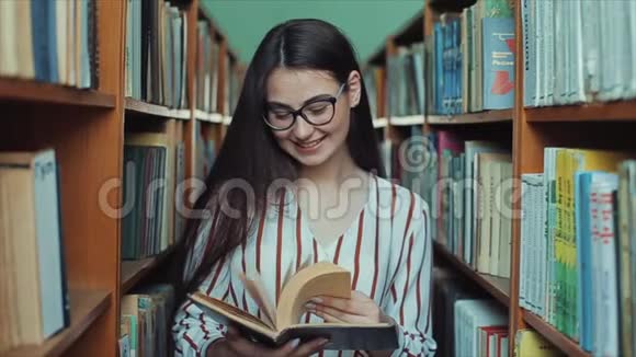 图书馆里戴着眼镜的年轻漂亮女人手里拿着一本书翻阅着书页女孩笑了视频的预览图