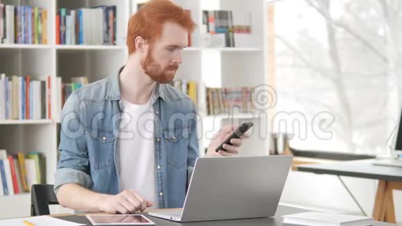 多任务休闲红发人使用电话平板电脑和笔记本电脑视频的预览图