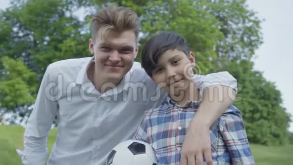 一位年轻父亲拥抱他儿子的肖像快乐的微笑男孩拿着足球家庭休闲户外活动父亲视频的预览图