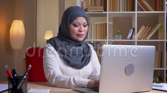 成年穆斯林女商人在室内工作场所用笔记本电脑打字时打哈欠和困倦的特写镜头视频的预览图