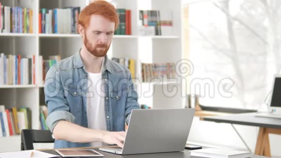 休闲红发男子背部疼痛在笔记本电脑上工作视频的预览图