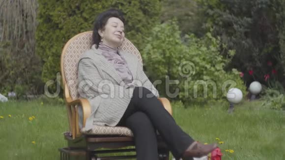 肖像成年女性坐在草地上摇椅上享受阳光特写成年孙子遮住眼睛视频的预览图